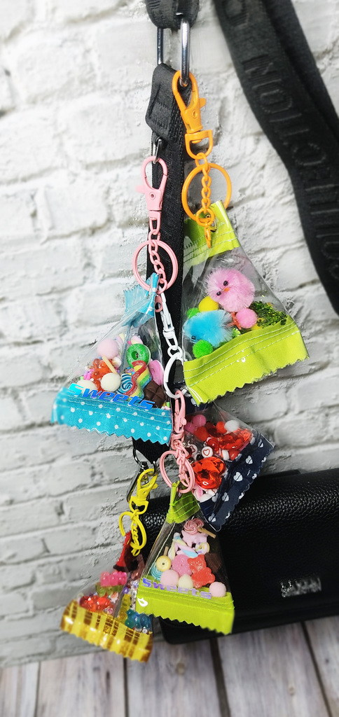 Bunte Schlüsselanhänger mit transparenten Taschen, gefüllt mit Fake Süssigkeiten und Statements, an einer Tasche befestigt.