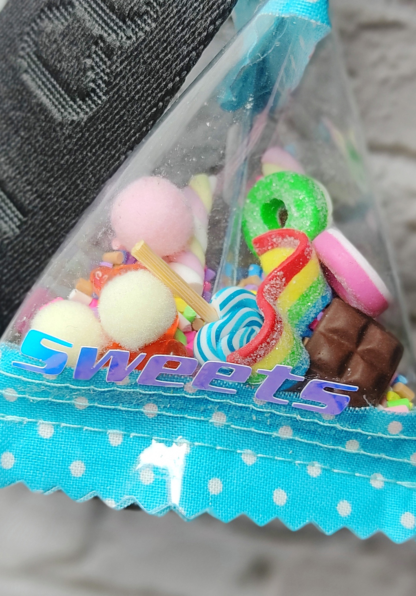 Eine Tüte voller bunter Fake-Süßigkeiten, darunter Gummibärchen, Lutscher, Schokolade und weitere Leckereien, mit einem Aufkleber mit der Aufschrift 'Sweets'.