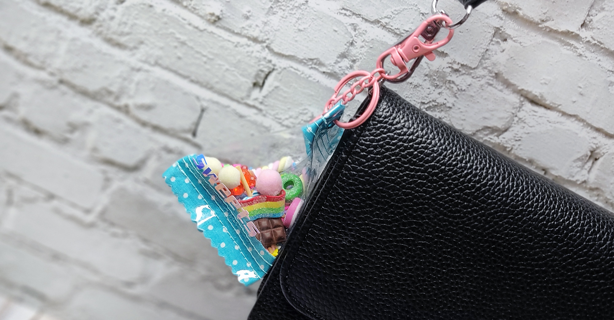 Schwarze Handtasche mit einem bunten, durchsichtigen Beutel voller Süßigkeiten.