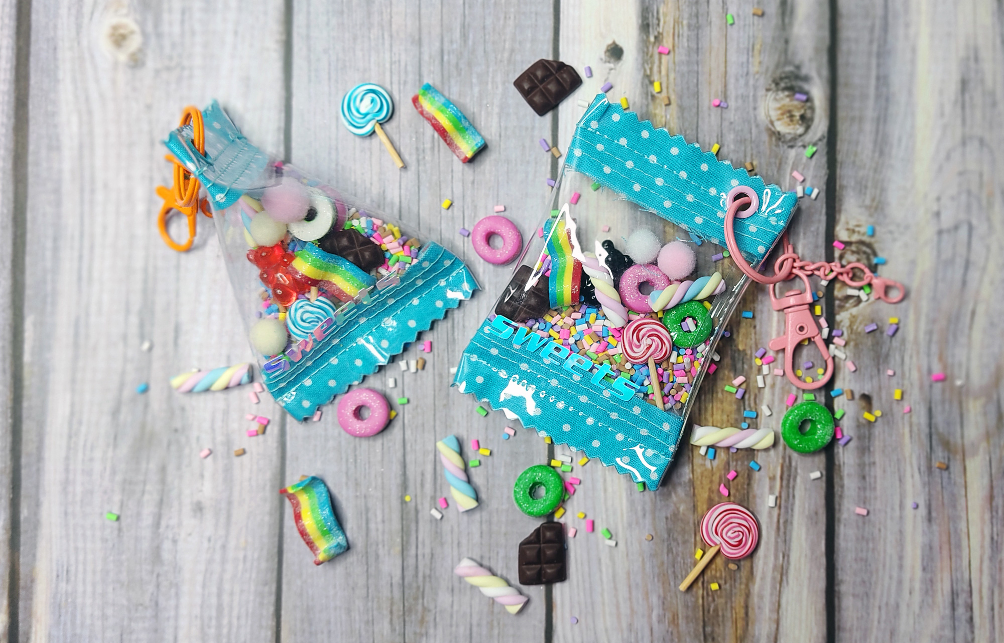 Zwei transparente Tüten mit bunten Süßigkeiten, darunter Gummibärchen, Lollis, Schokolade, und bunte Donuts, auf einem Holzuntergrund drapiert.